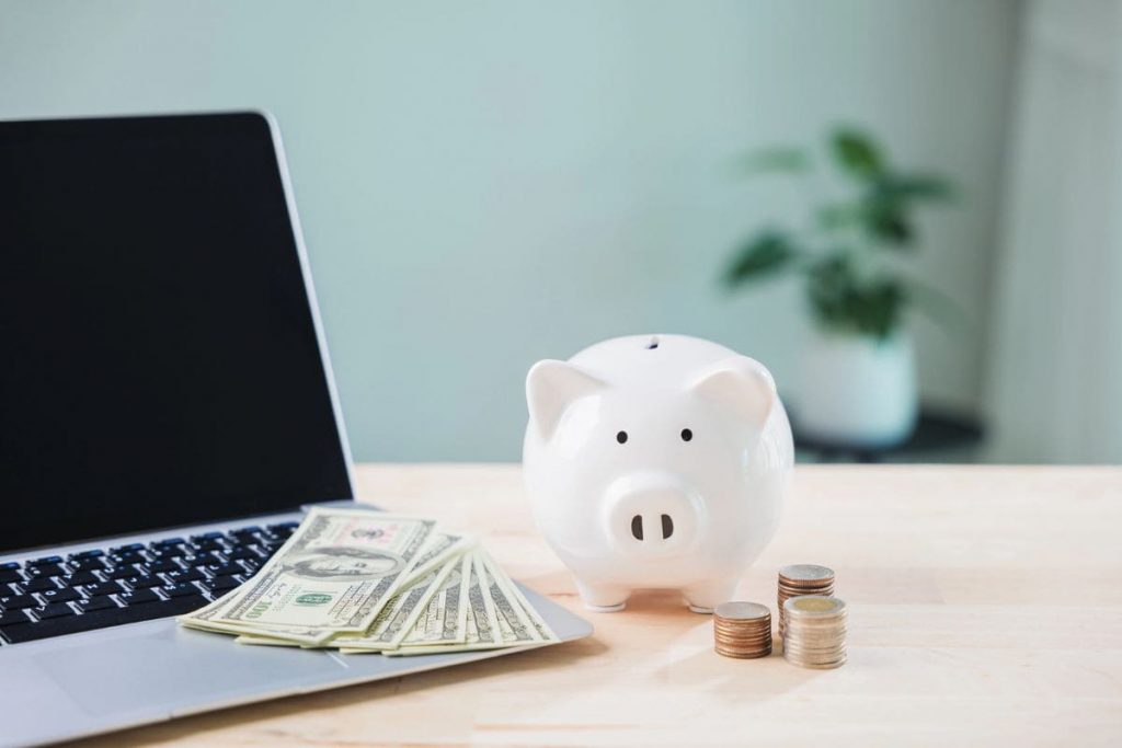 A home office desk, with a laptop and piggy bank.