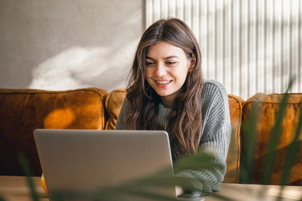 Woman working from home on a couch, using a laptop.
