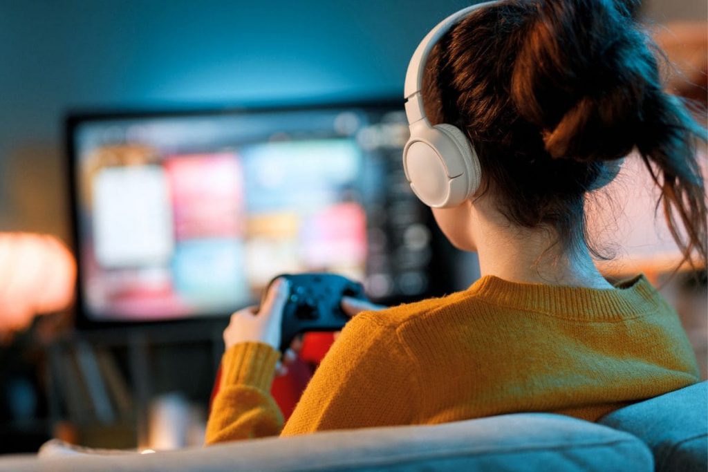 A woman sitting on a couch, playing video games in her living room.