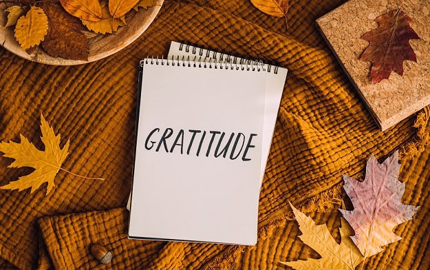 The Power of Thankfulness: 5 Helpful Tips A notebook with the word gratitude written on it and fall leaves around the notebook.
