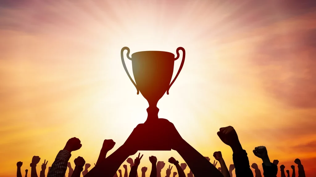 D-Wave Quantum Is Looking Like The Early Quantum Computing Winner (Upgrade) (NYSE:QBTS) Silhouette of many hands raised with trophy on sunset background.