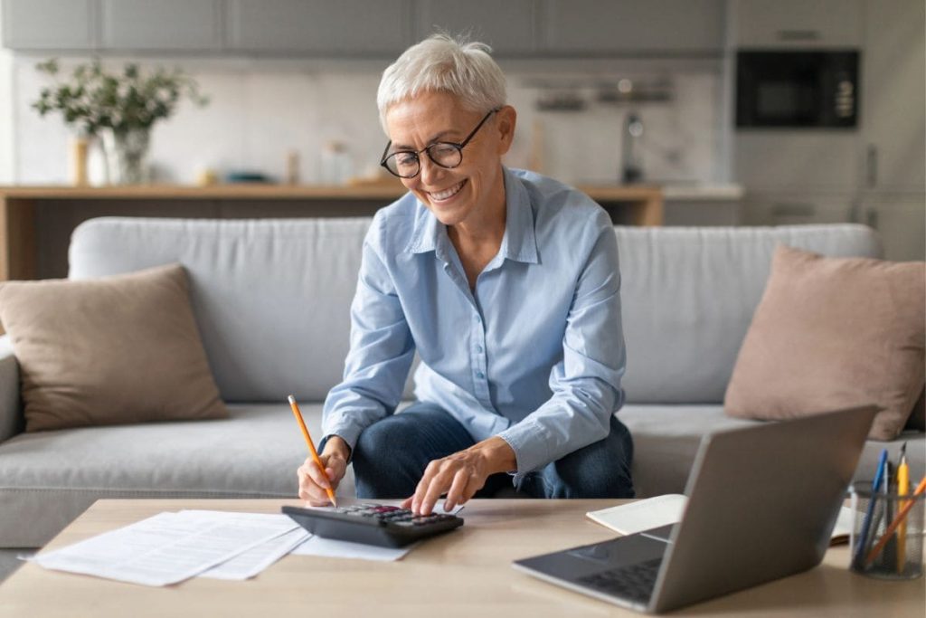 A woman working from home on her couch, using a laptop and calculator.