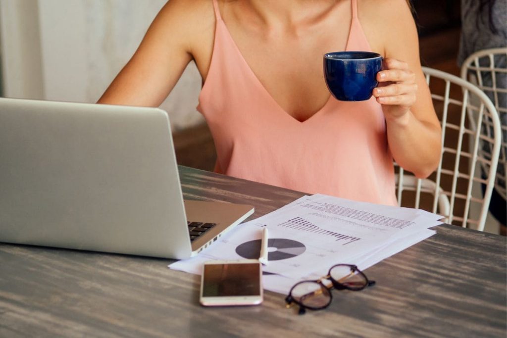 A woman working from home and drinking coffee at her computer.