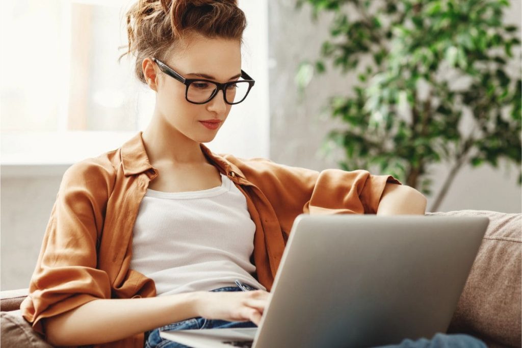 A woman sits on her couch, using her laptop to browse second income opportunities online.