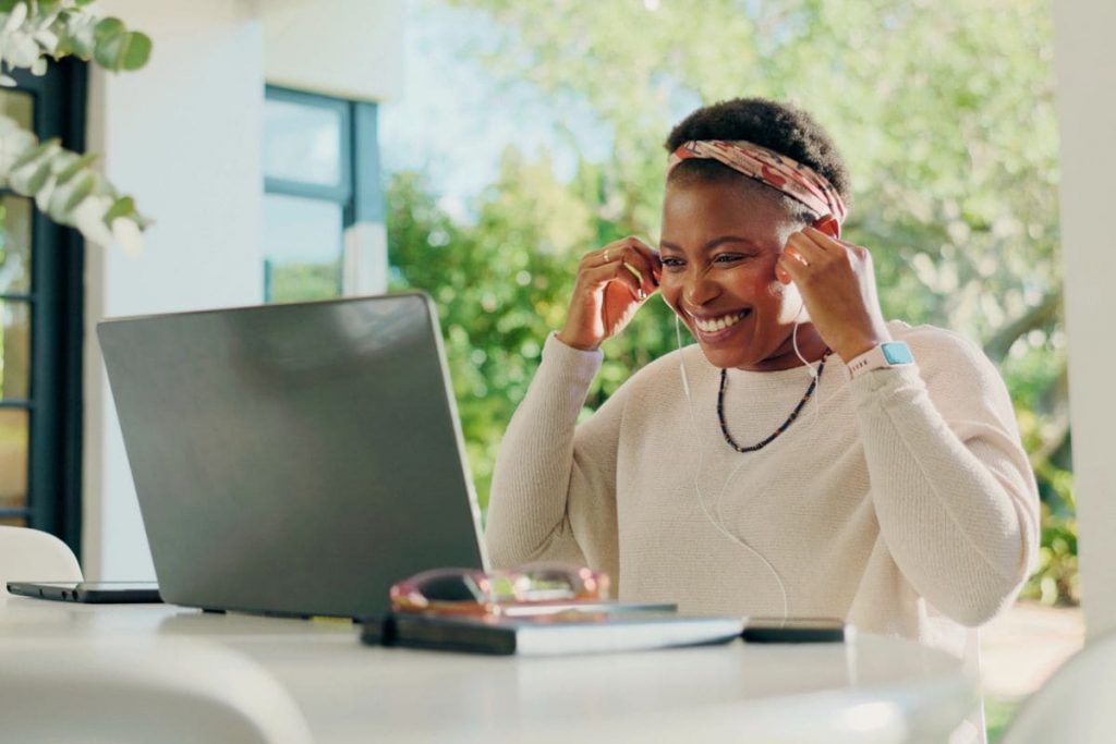 A woman working remotely from an outdoor table, putting on earphone to take a virtual call.