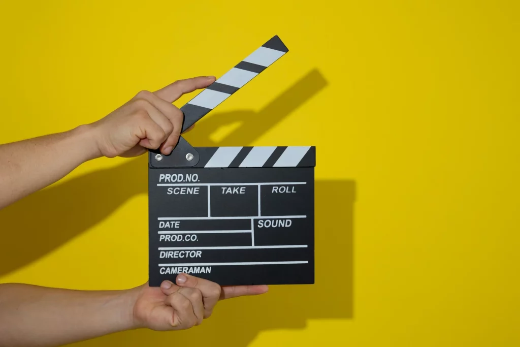 Mãos segurando uma claquete de filme em um fundo amarelo