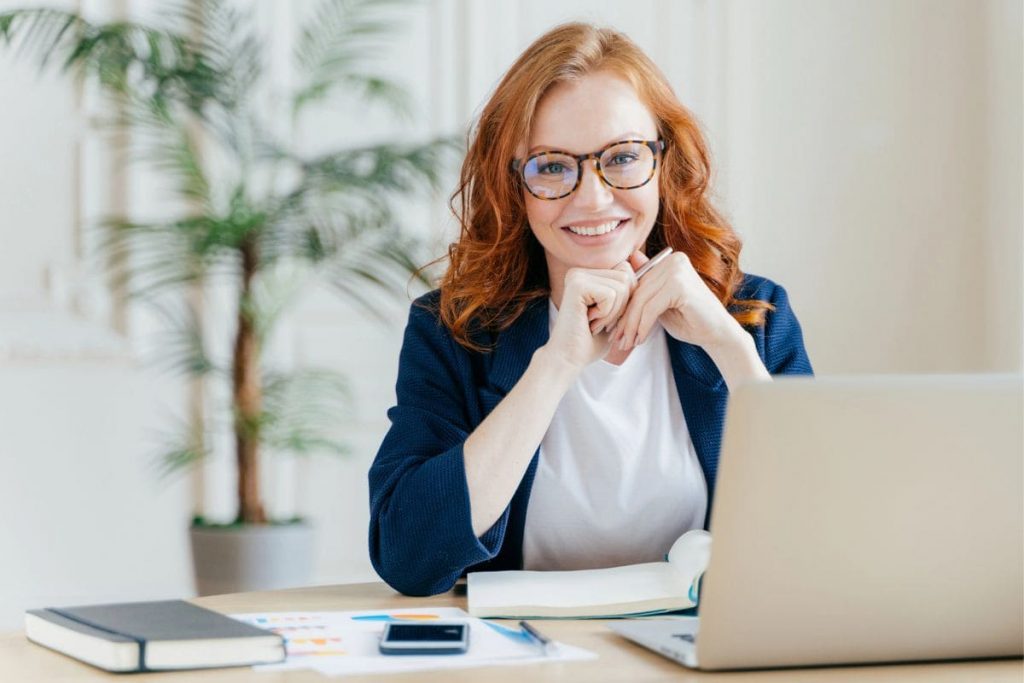 A woman business owner, smiling and sitting at her home office desk.