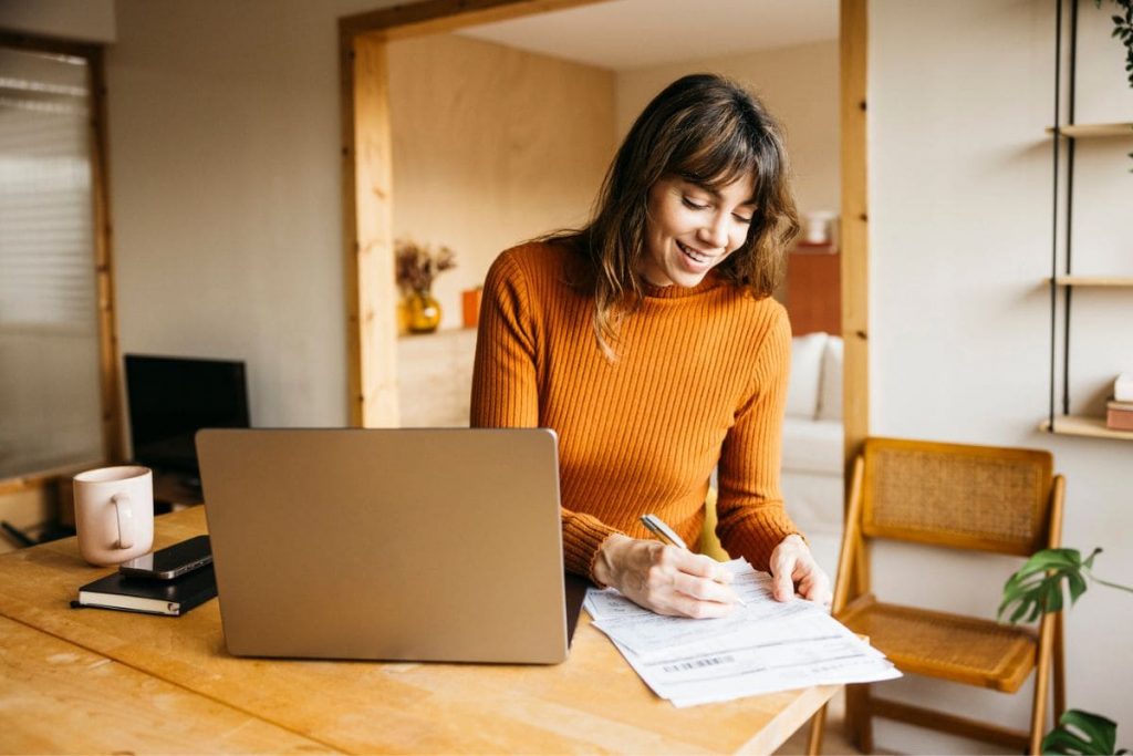 12 Interesting and Fun Remote Jobs for English Majors A woman working remotely from her home office desk, using a laptop and writing in a notebook.
