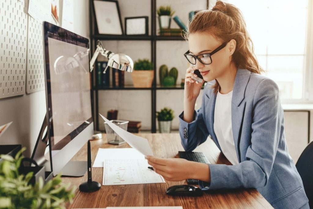 10 Top High-Paying Entry-Level Jobs You Can Do From Home A woman working remotely from her home office, using a desktop computer and talking on a cell phone.