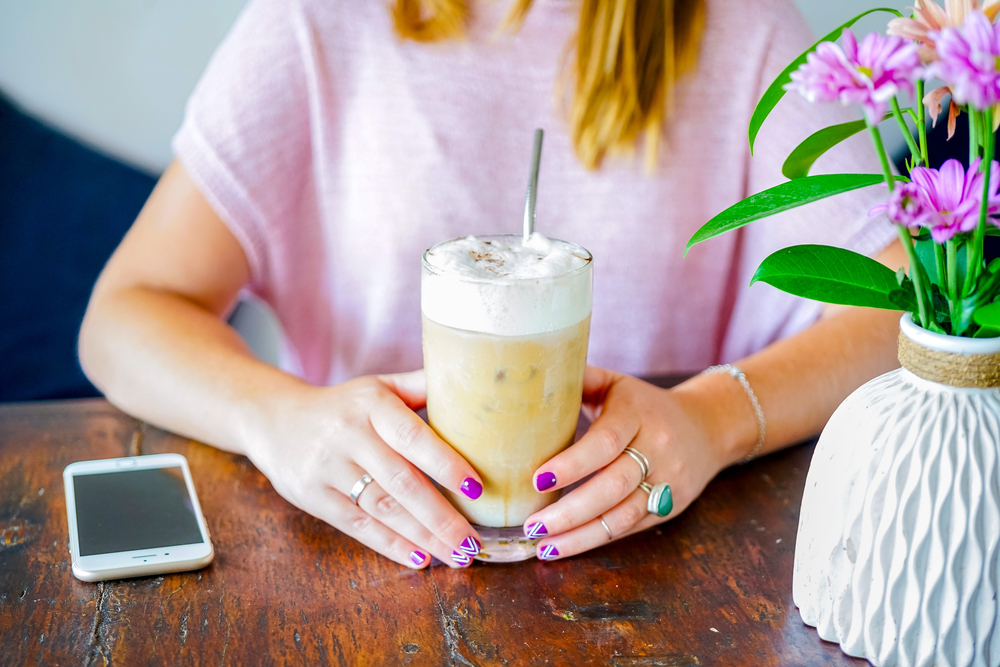 12 Ways to Earn FREE Starbucks Gift Cards and Coffee Young woman with painted finger nails drinking an iced coffee in a coffee shop for blog post free starbucks gift cards