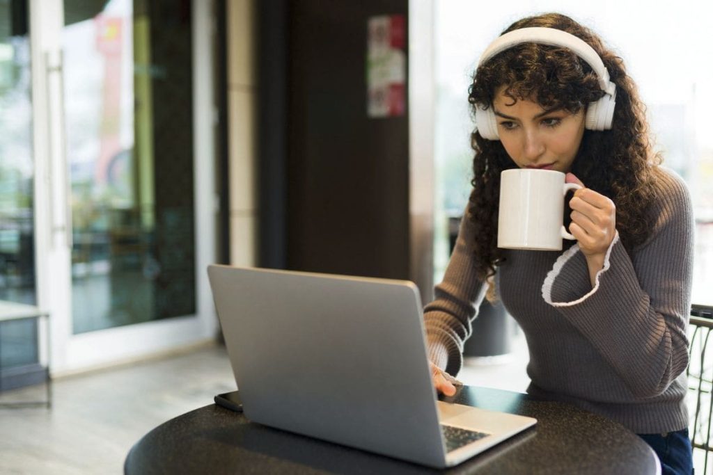 14 Quiet Remote Jobs That Don’t Require Talking on the Phone A woman working quietly in a cafe, using a laptop and drinking coffee.